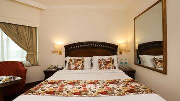 Een hotelkamer met een groot bed, een bloemenprint beddeken, twee bedlampjes, een nachtkastje met een telefoon en een spiegel aan de muur.
