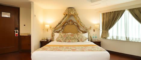 Una habitación de hotel con una cama grande, dosel, dos mesitas de noche con lámparas, piso de madera y una ventana con cortinas.