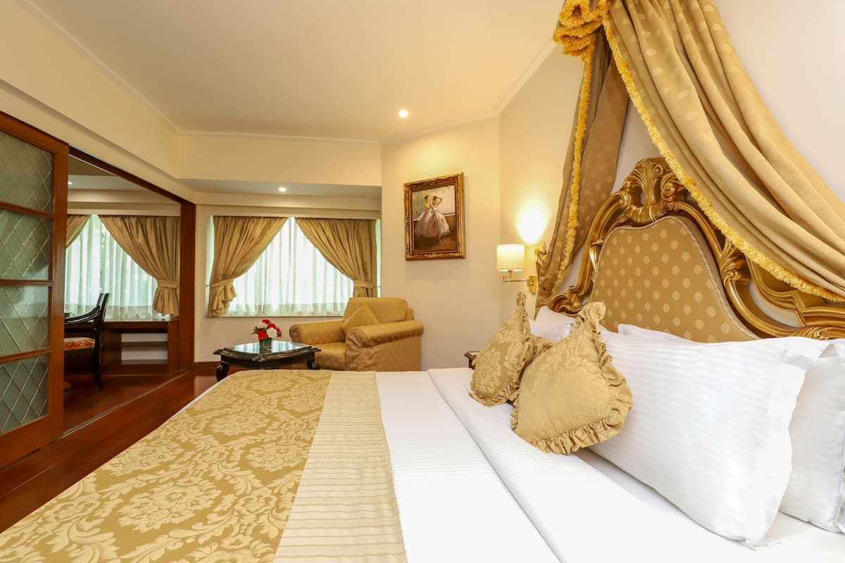A hotel room with a large bed, a sitting area with a sofa and armchairs, a small table, and a painting on the wall.