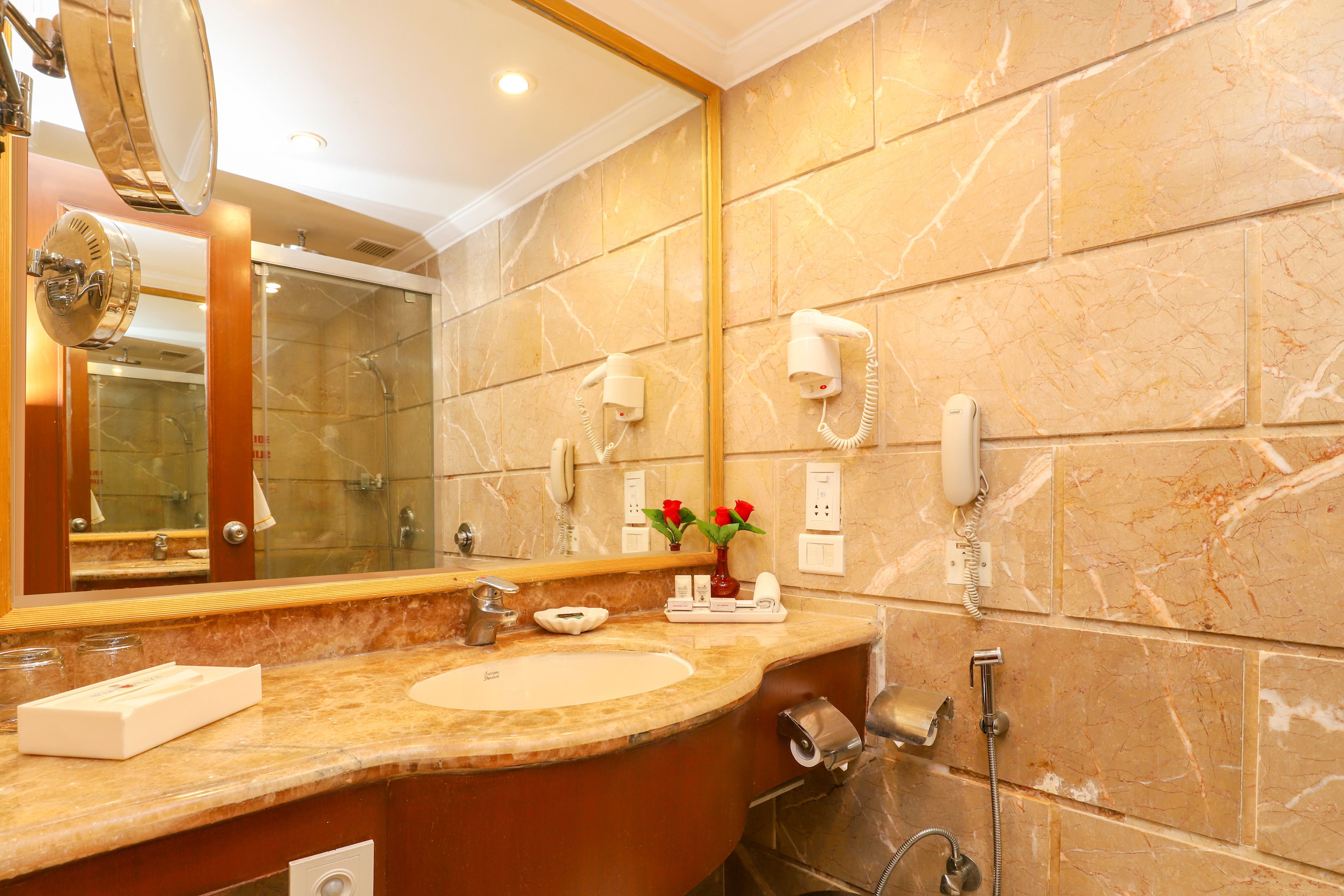 Un baño con encimera de mármol, un espejo grande, un lavabo, tocador, ducha y teléfono.