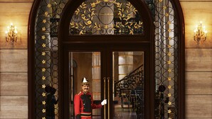 A grand entrance with a guard, a staircase, and a chandelier.