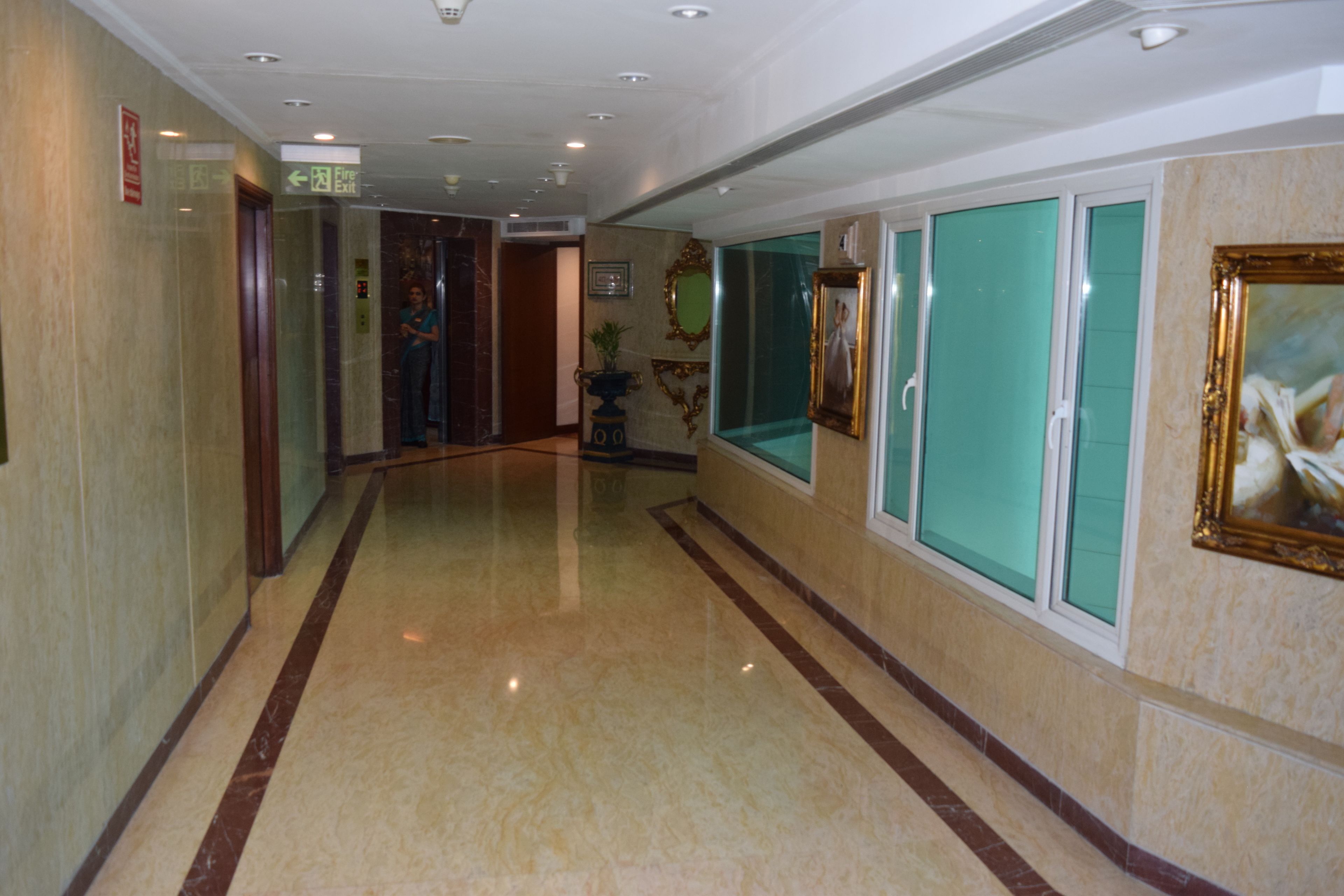 Un pasillo de hotel con pisos de mármol, puertas de cristal y cuadros en las paredes.