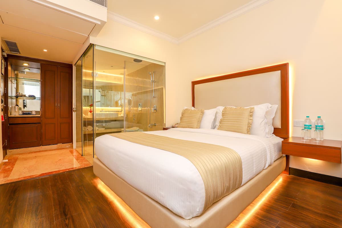 A hotel room with a large bed, a glass-enclosed shower, wooden furniture, and a nightstand with water bottles.