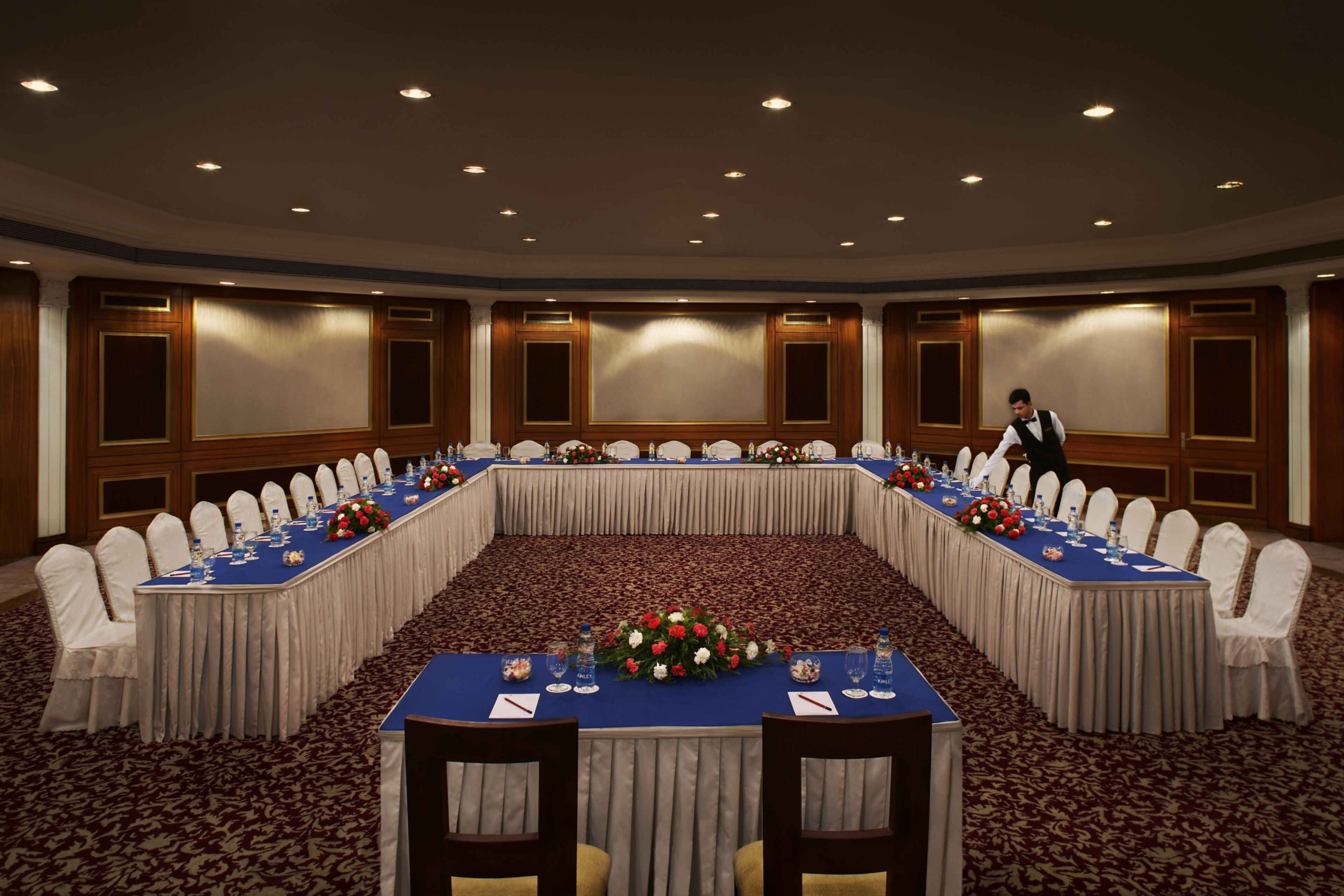 Une salle de conférence avec une longue table, des chaises blanches et un sol recouvert de moquette.
