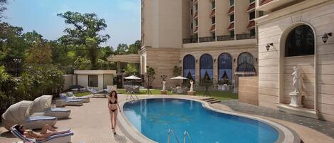 A swimming pool with lounge chairs, a statue, and a building with arched windows.