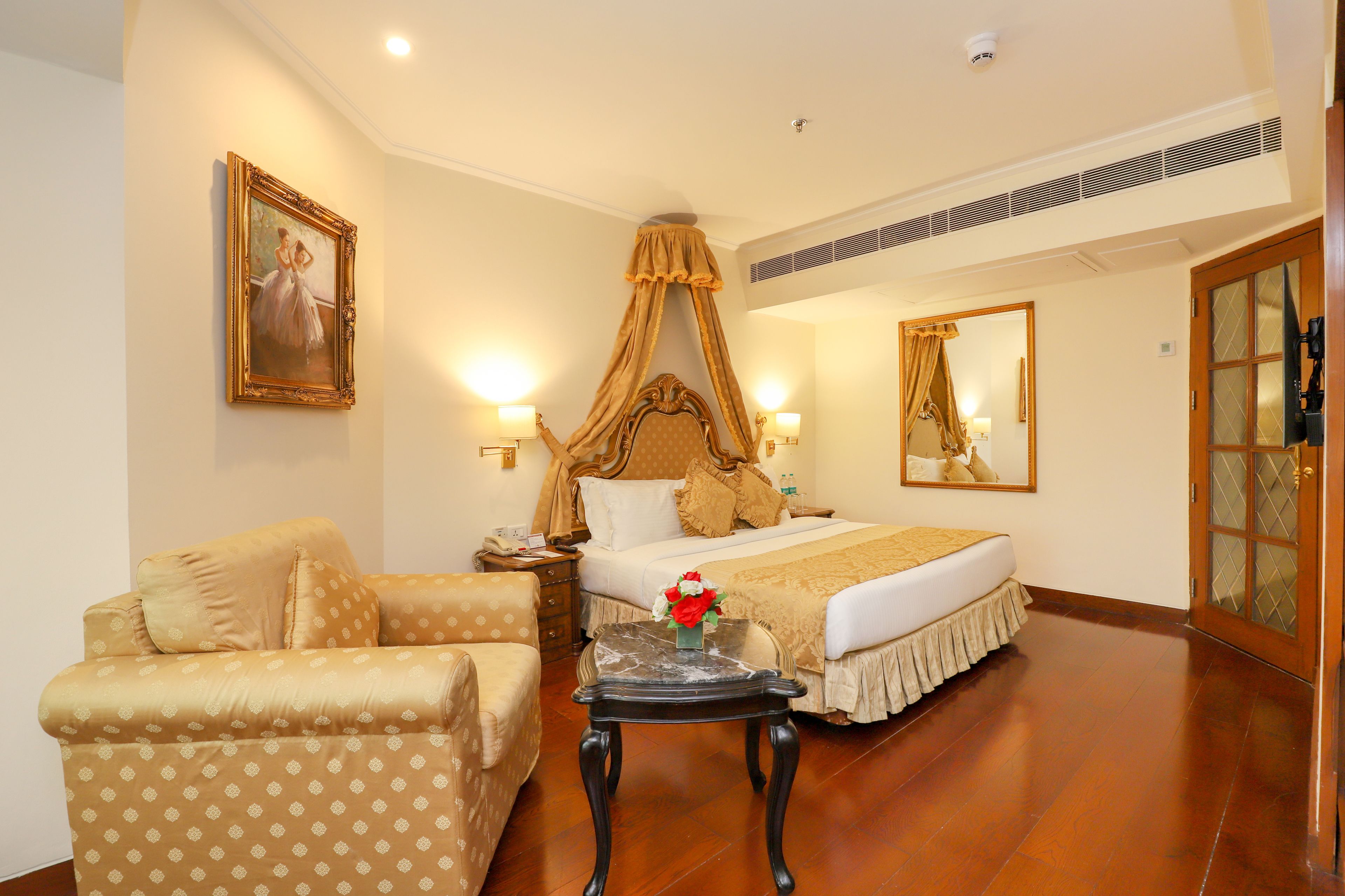 A hotel room with a large bed, a sitting area with a sofa, a nightstand, and a painting on the wall.