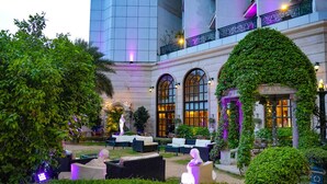 An outdoor seating area with wicker furniture, a statue, and a well-maintained garden.
