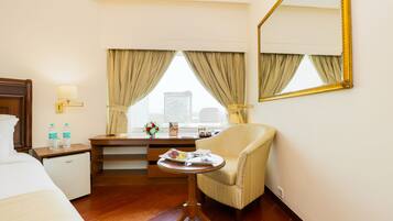 A hotel room with a bed, a desk with a lamp, a chair, a small table with a tray, and a large mirror on the wall.