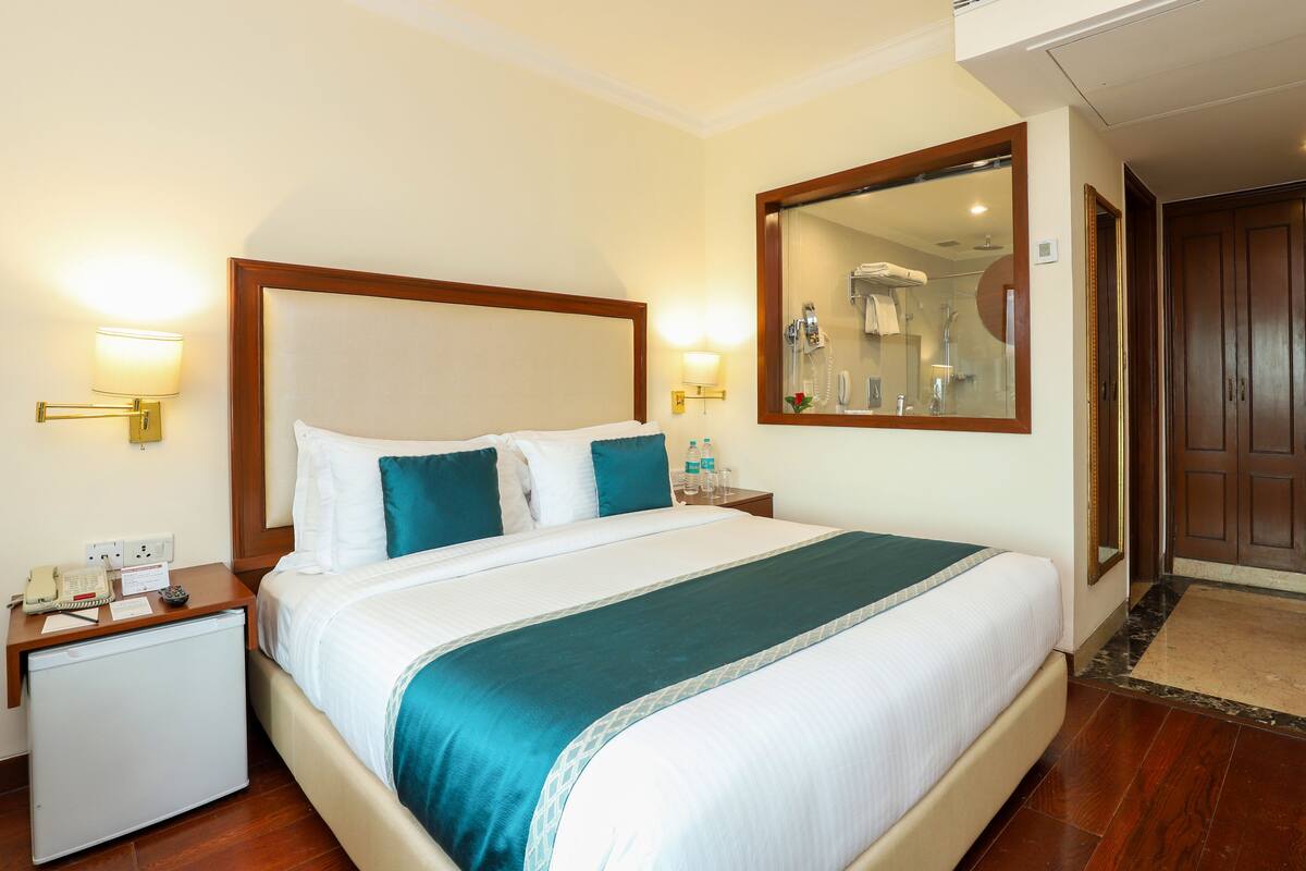 A hotel room with a bed, bedside lamps, a nightstand, a mirror, and a door.