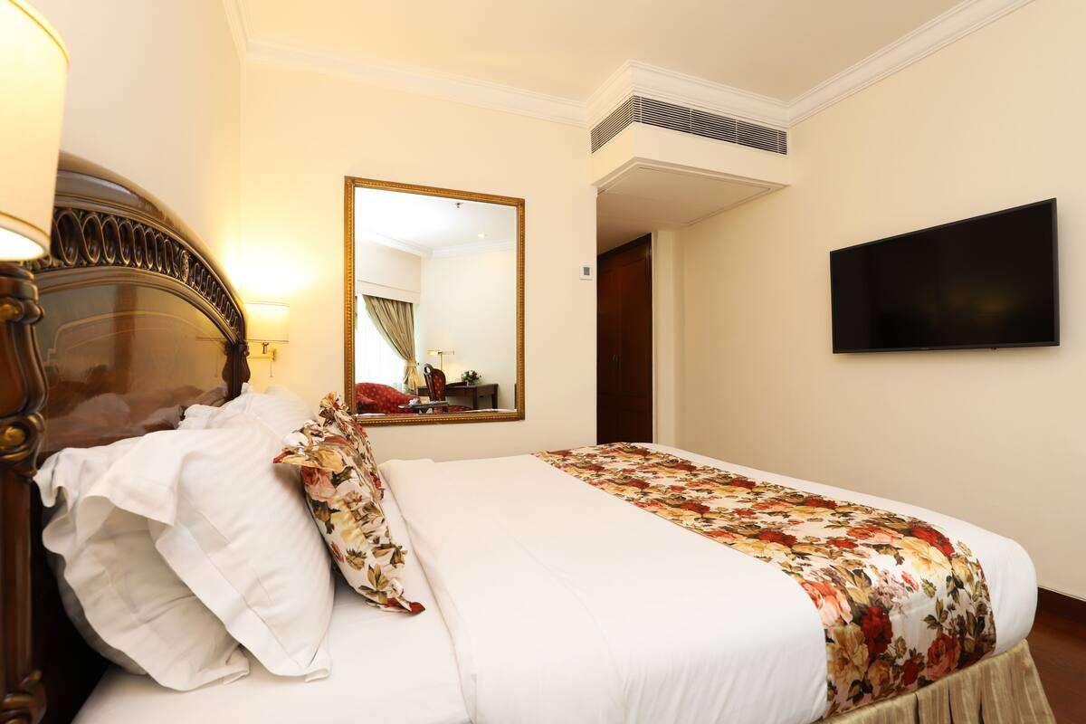A hotel room with a bed, a mirror, a flat-screen TV, and a door leading to another room.