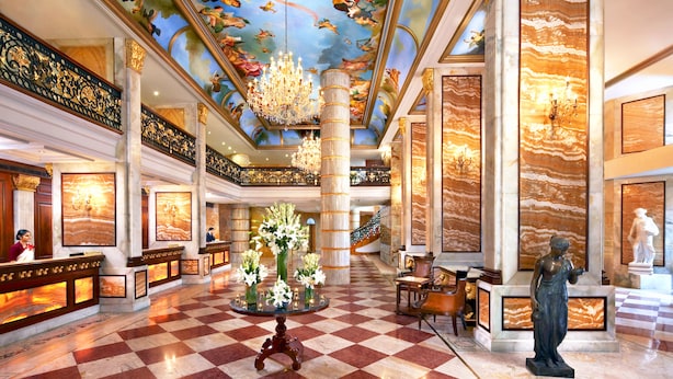 A grand lobby with a checkered floor, a central floral arrangement, and a statue.