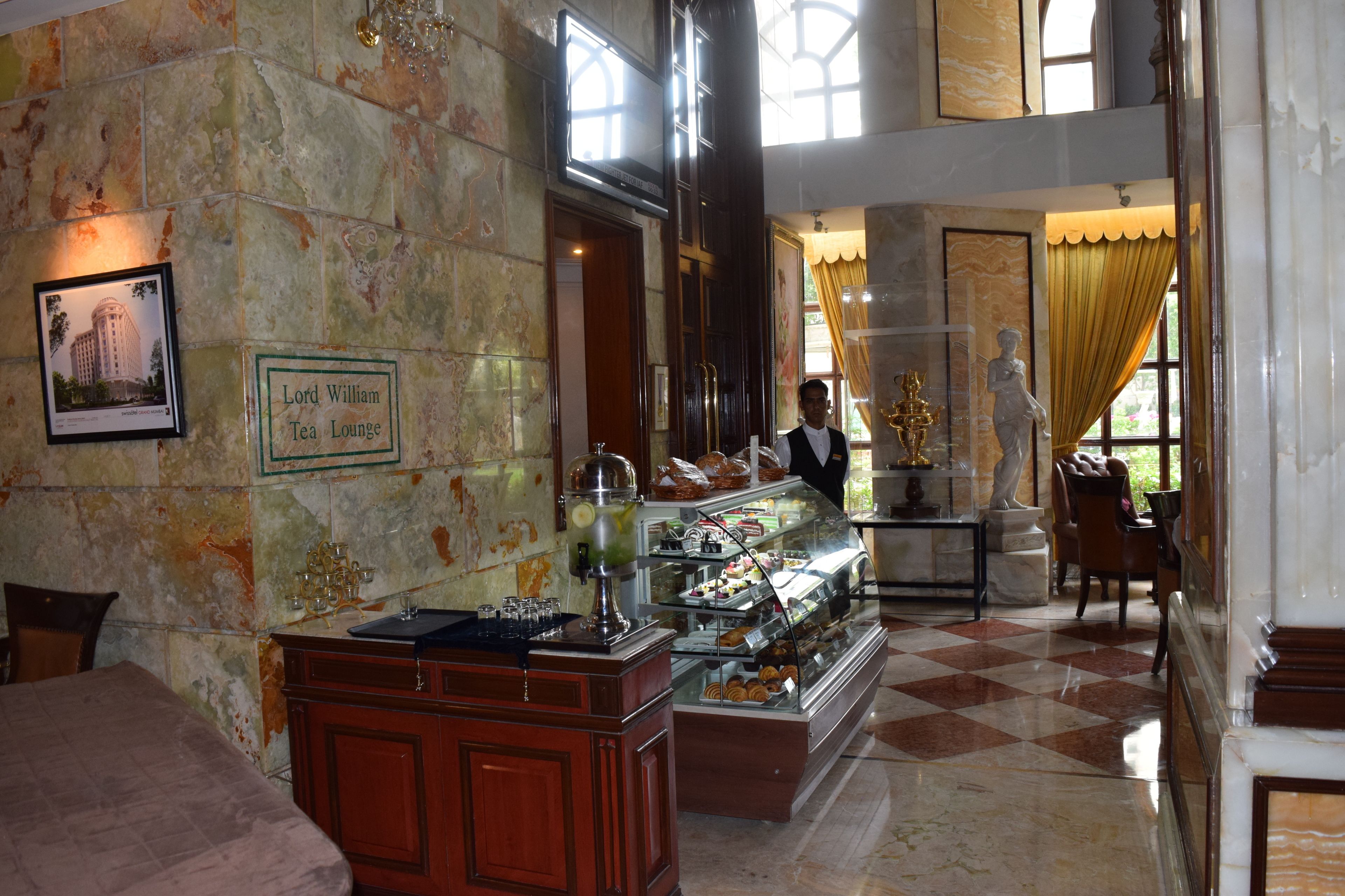 Un salon de thé avec un mur en marbre, un buffet proposant des pâtisseries et une statue.