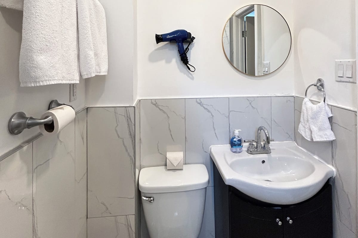 Un baño con inodoro, lavabo, toallero y secador de pelo fijado en la pared.