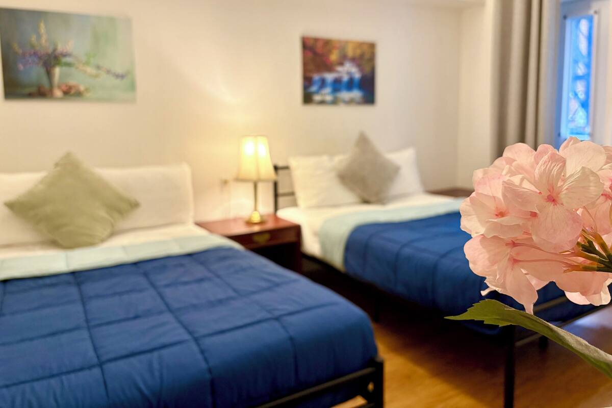 Habitación de hotel con dos camas, una mesita de noche con lámpara y obras de arte en las paredes.