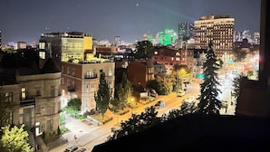 Paisagem urbana noturna com edifícios, um estacionamento e uma rua com carros.