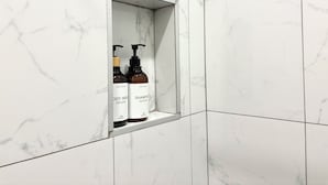 Casa de banho com azulejos de mármore branco e uma prateleira com dois frascos de gel de banho e shampoo.
