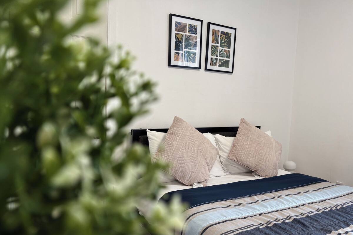 Un dormitorio con una cama, almohadas, una colcha y dos cuadros en la pared.
