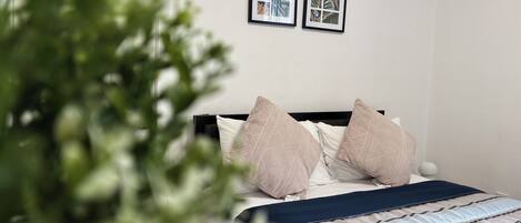A bedroom with a bed, pillows, a blanket, and two framed pictures on the wall.