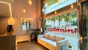 A modern lobby with a sofa, a reception desk, a large window with a view of the street, and pendant lighting.