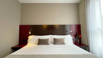 Una habitación de hotel con una cama grande, dos lámparas de noche, una mesita de noche y un florero con flores.