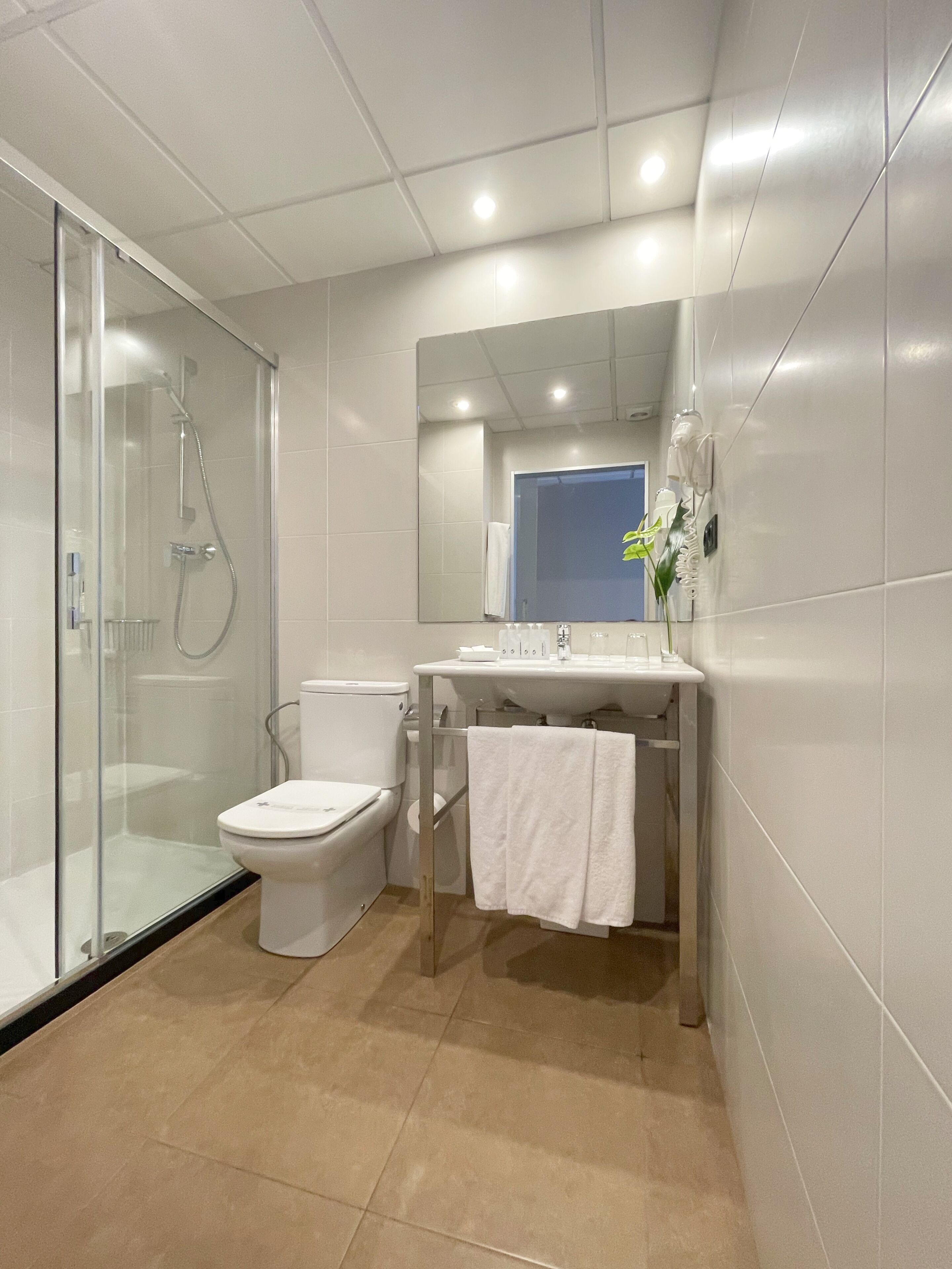 Un baño moderno con cabina de ducha de vidrio, inodoro y lavamanos con espejo superior.