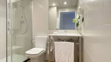 Un baño moderno con cabina de ducha de vidrio, inodoro y lavamanos con espejo superior.