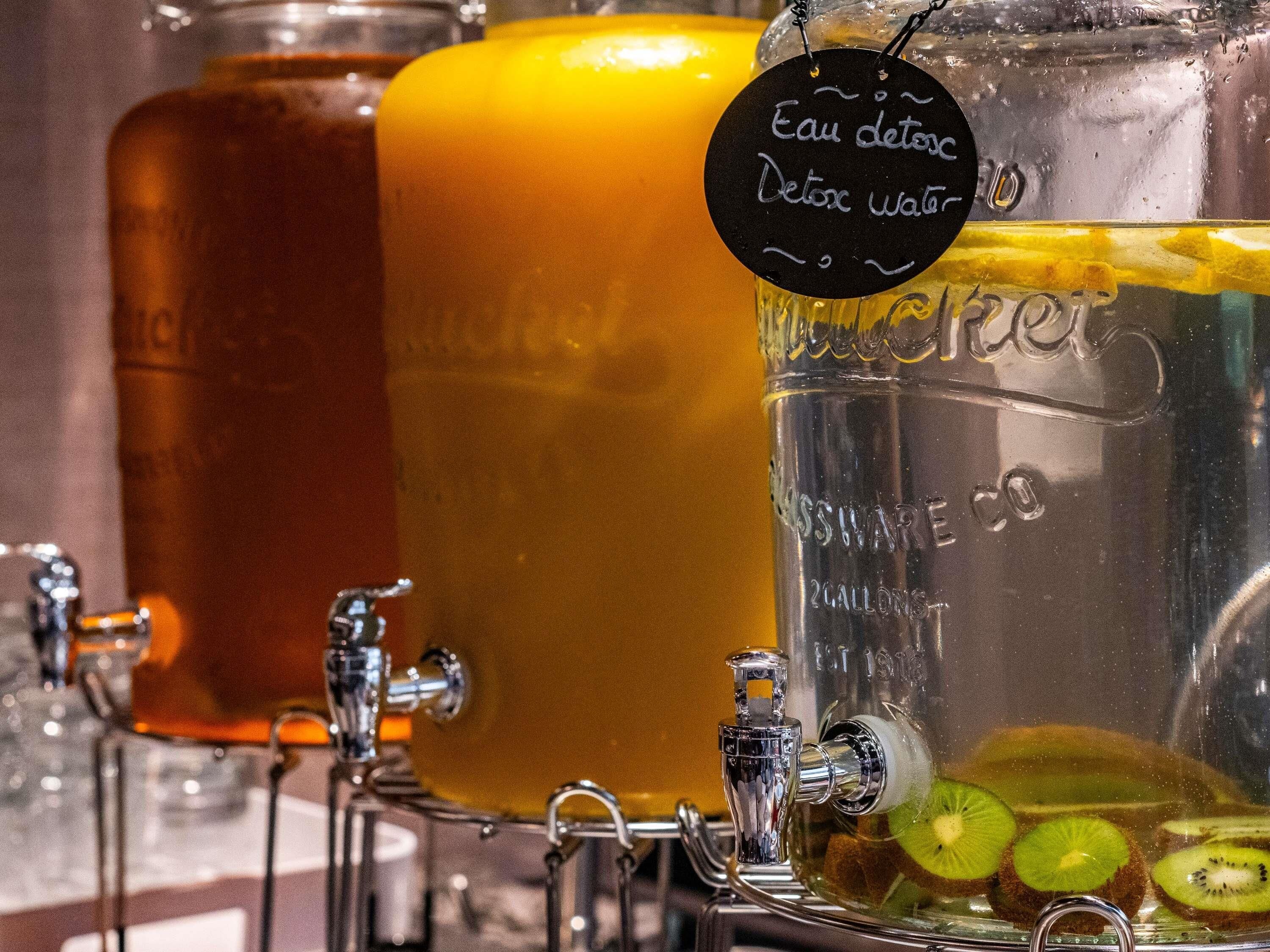 Un dispensador de bebidas con una etiqueta negra que dice "Eau Detox" y un recipiente de vidrio con rodajas de kiwi.