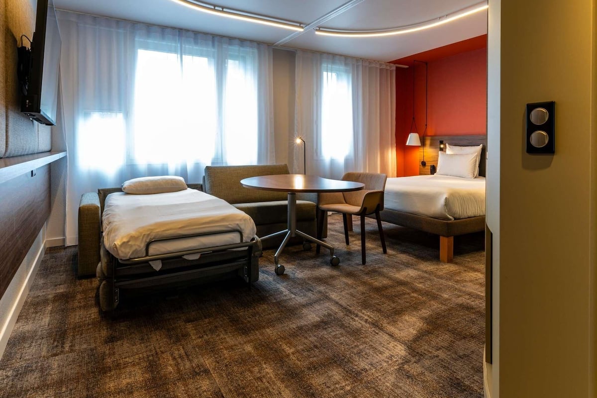 A hotel room with a bed, a desk, a chair, a TV, and a window with curtains.