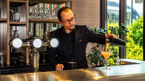 A bartender pouring a drink into a martini glass at a bar with a view of greenery outside. - Novotel Suites Reims Centre (Reims)