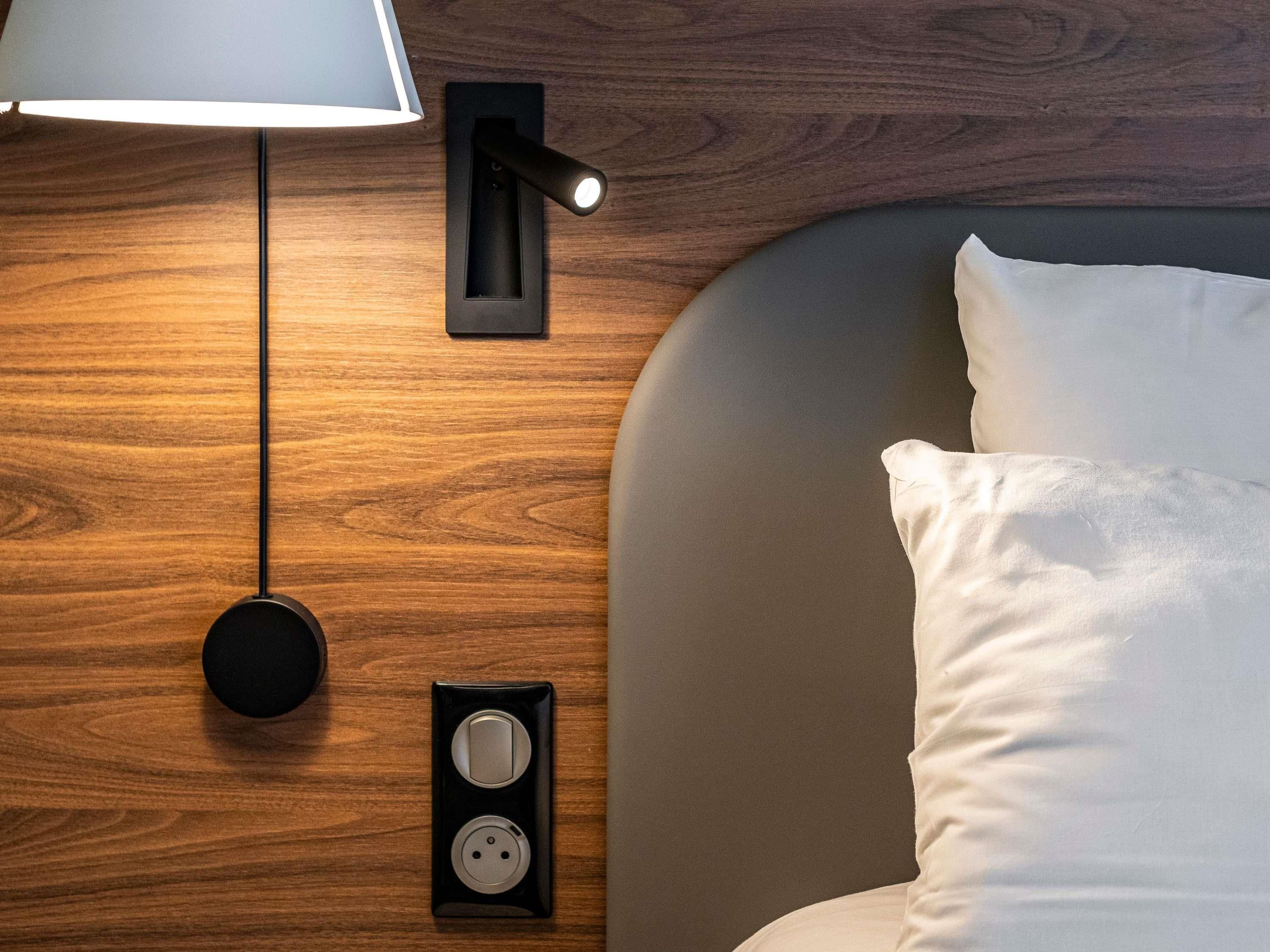 Una cama bien hecha con cabecera, una lámpara de pared y un enchufe.