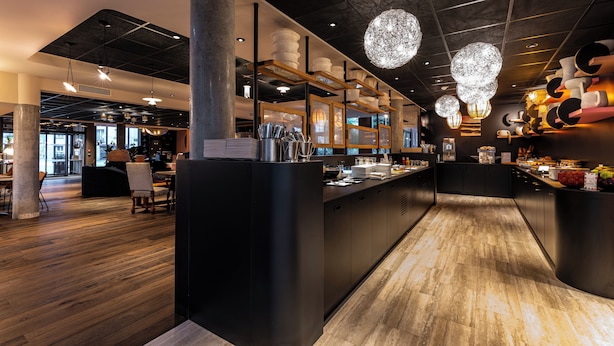 Interior moderno de restaurante con mostrador central, suelo de madera y lámparas esféricas colgantes.