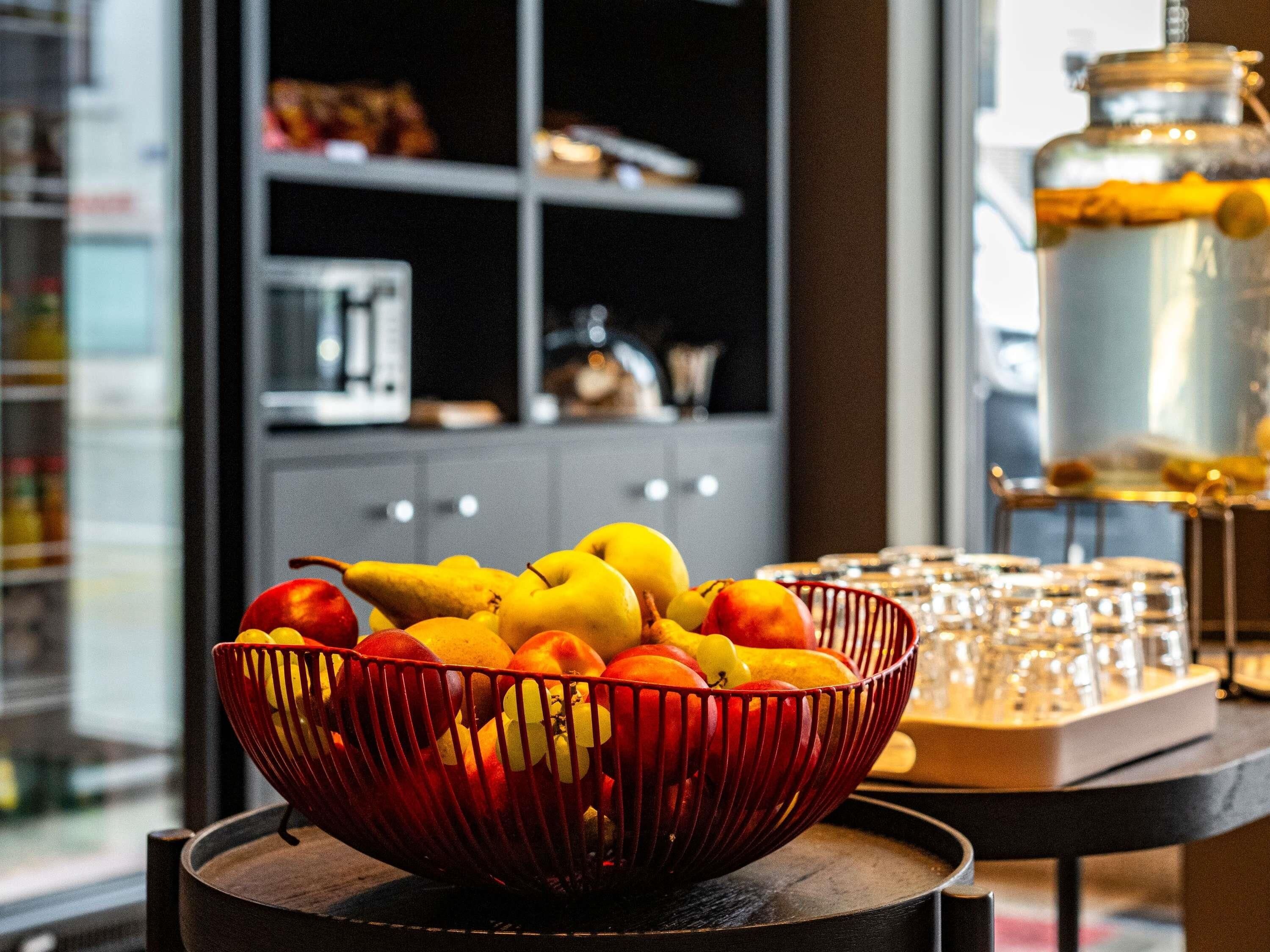 Un frutero sobre una mesa, con una cocina al fondo.