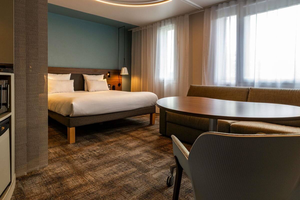 Hotellihuone, jossa on sänky, sohva, pyöreä pöytä ja työpöytä.