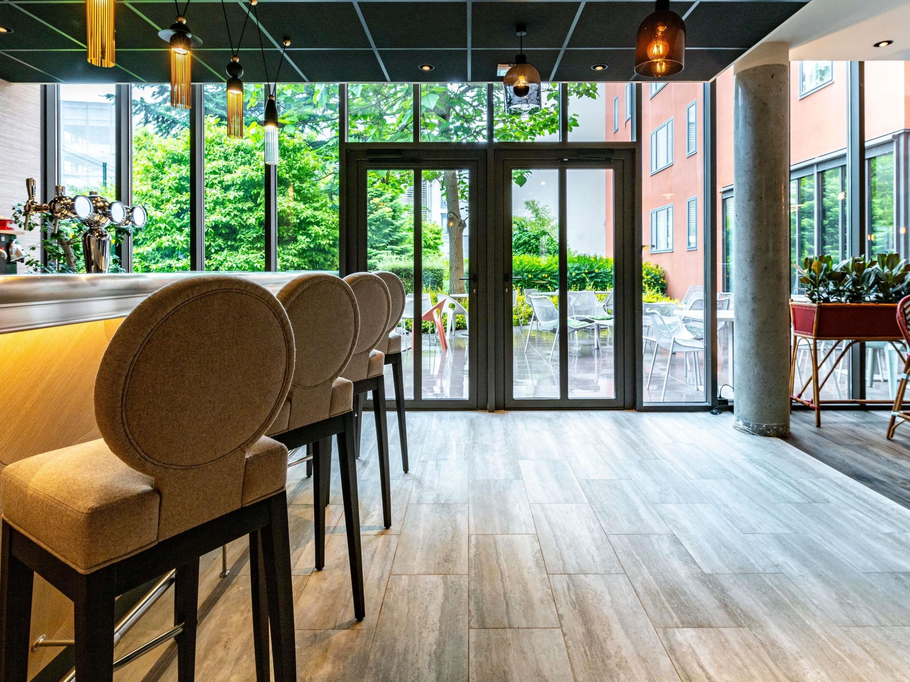 Ein moderner Barbereich mit einer langen Theke, mehreren Barhocker und großen Fenstern mit Blick ins Freie.
