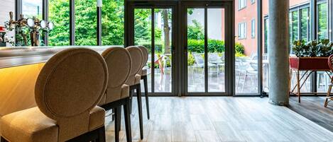 A modern bar area with a long counter, multiple bar stools, and large windows offering a view of the outdoors.