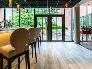 A modern bar area with a long counter, multiple bar stools, and large windows offering a view of the outdoors. - Novotel Suites Reims Centre (Reims)