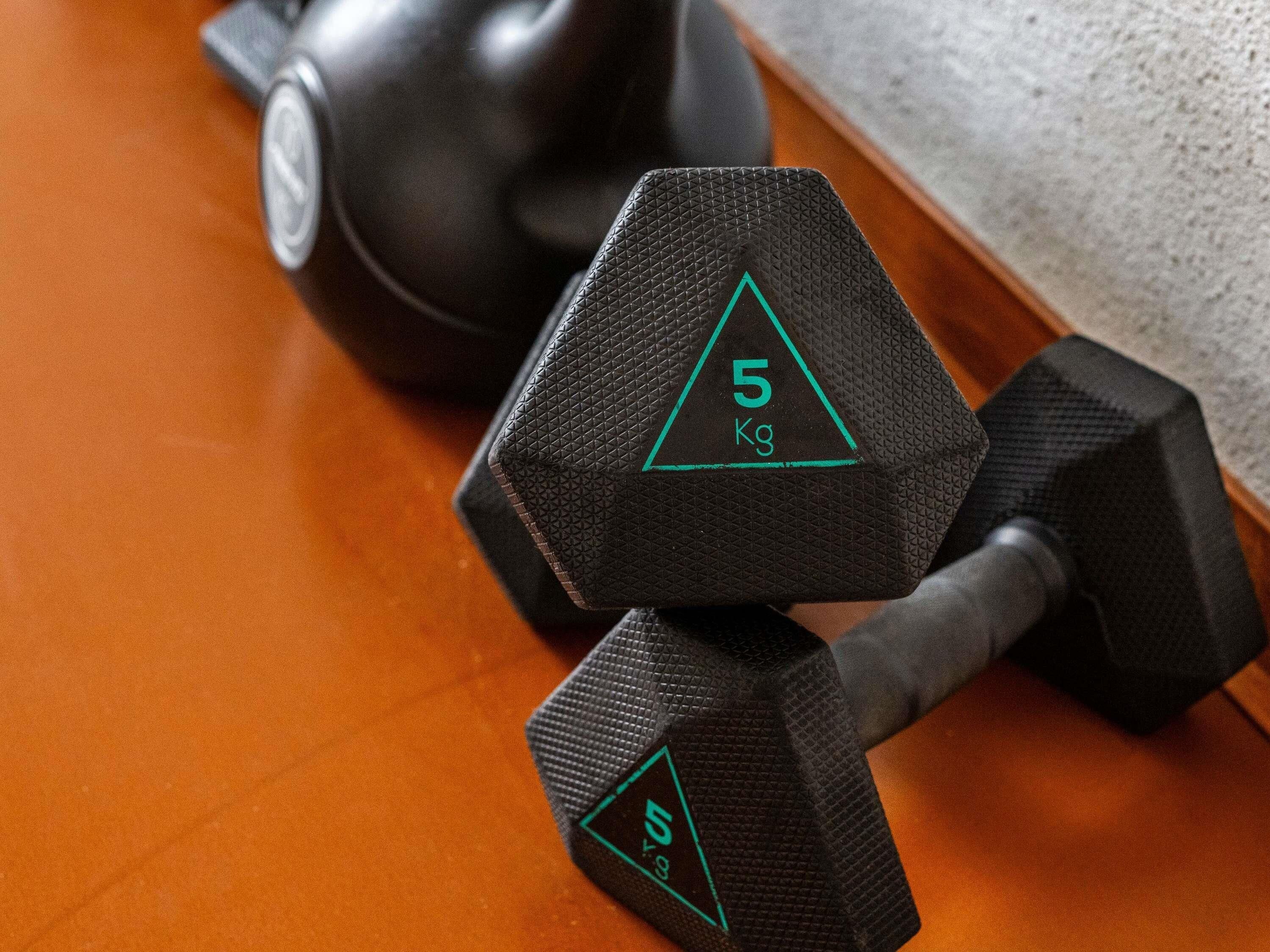 Two black dumbbells with a green triangle and the number 5 on them, placed on a wooden floor.