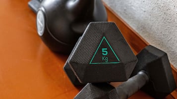 Two black dumbbells with a green triangle and the number 5 on them, placed on a wooden floor.