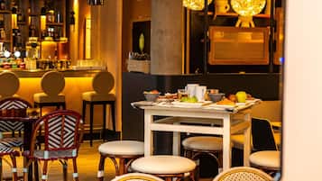L’intérieur d’un restaurant avec des chaises en osier, une table blanche dressée et des lampes suspendues.