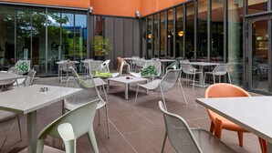 An outdoor seating area with tables and chairs, large windows, and a building with orange walls. - Novotel Suites Reims Centre (Reims)