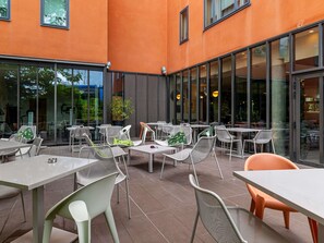 An outdoor seating area with tables and chairs, large windows, and a building with orange walls. - Novotel Suites Reims Centre (Reims)