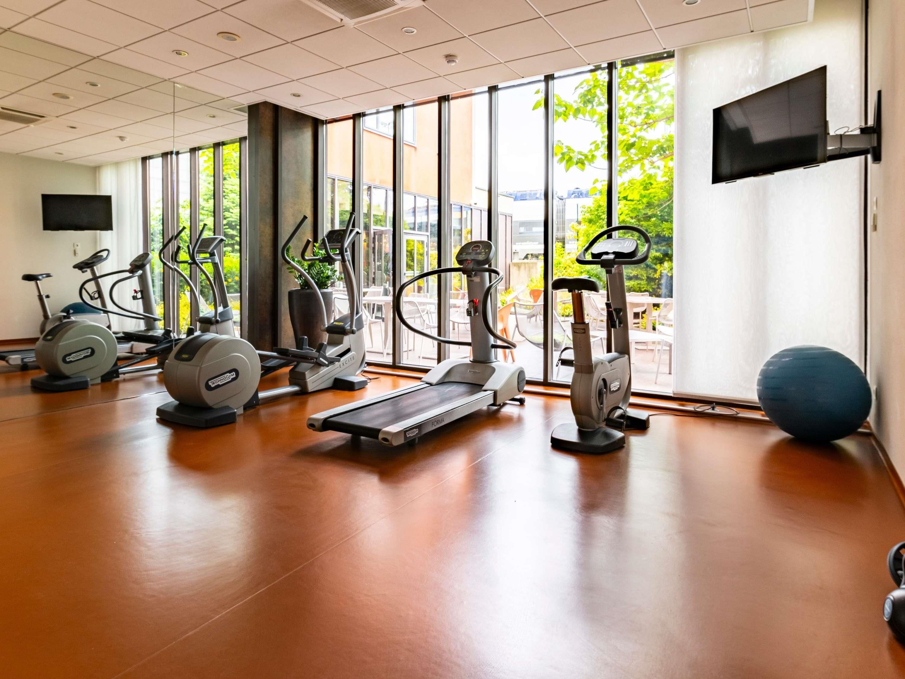 Un gimnasio con máquinas de cardio, cinta de correr y una pelota de ejercicio grande.