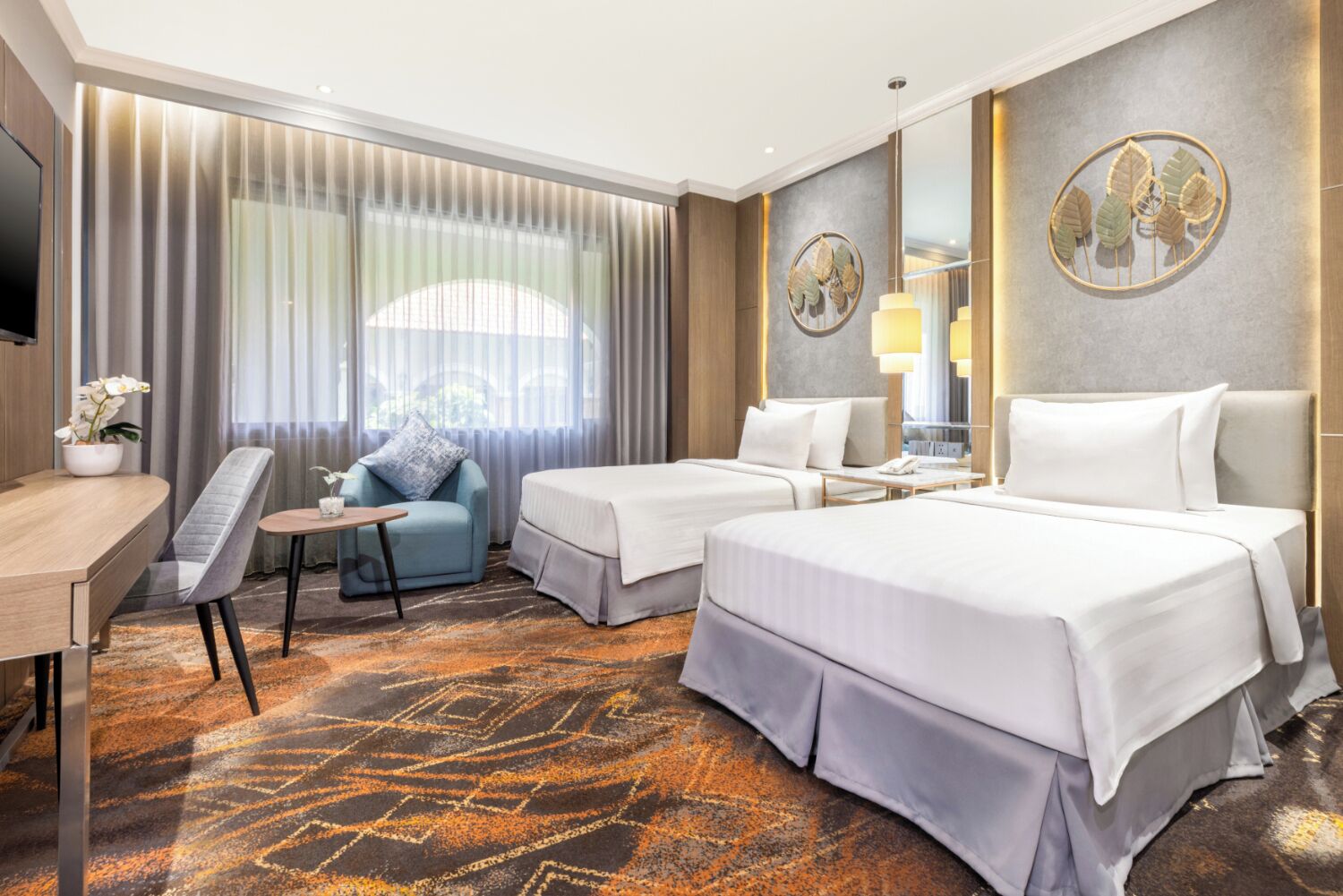 A hotel room with two beds, a desk, a chair, and a large window with curtains.