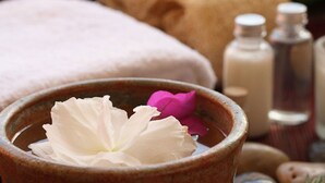 Een spa-omgeving met een kom waarin een witte bloem en een roze bloem liggen, omringd door kaarsen en spa-producten.