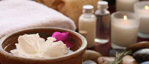 A spa setting with a bowl containing a white flower and a pink flower, surrounded by candles and spa products. - Aston Tropicana (Bandung)