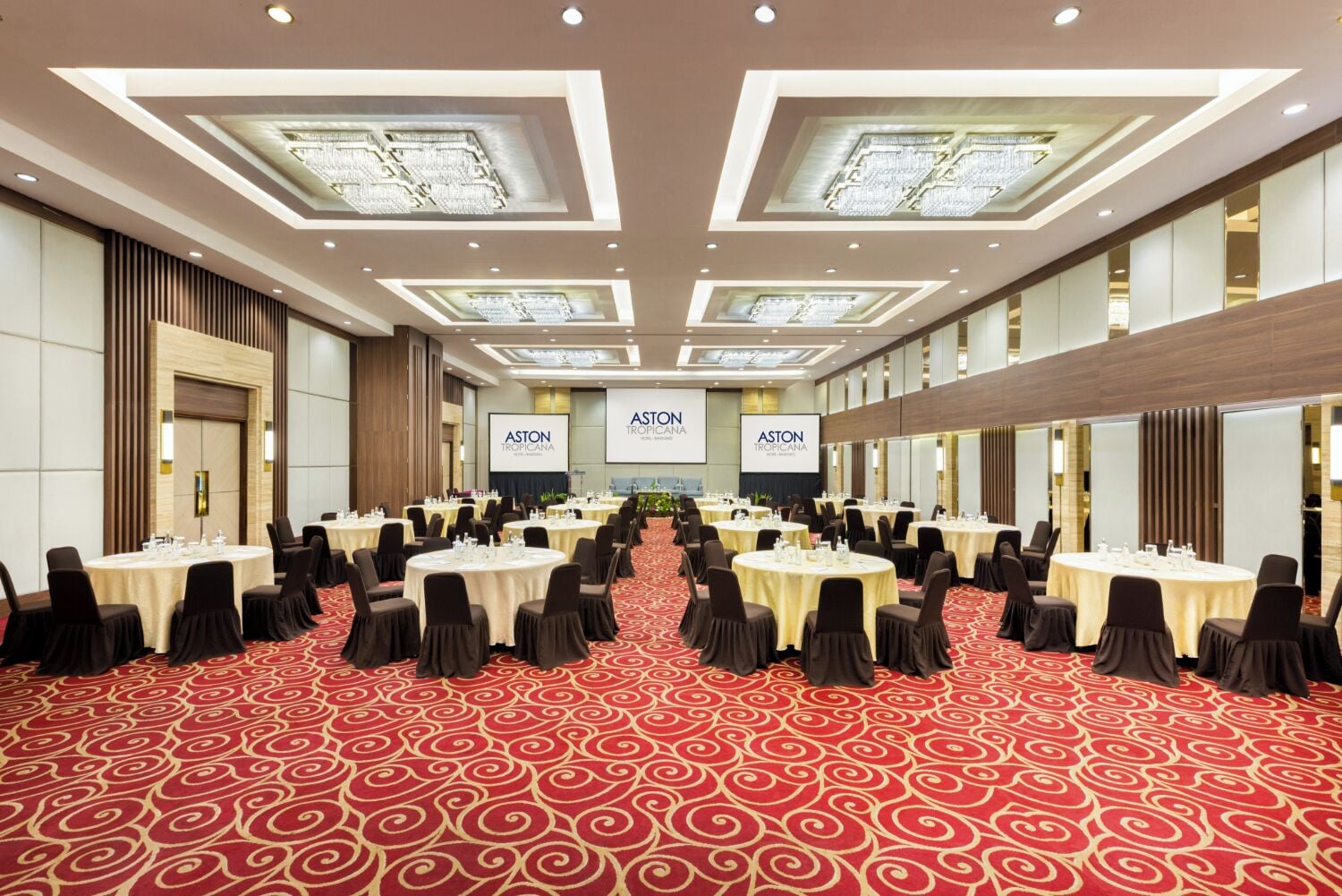 A large conference room with multiple round tables, black chairs, and a red carpet with a swirl pattern.