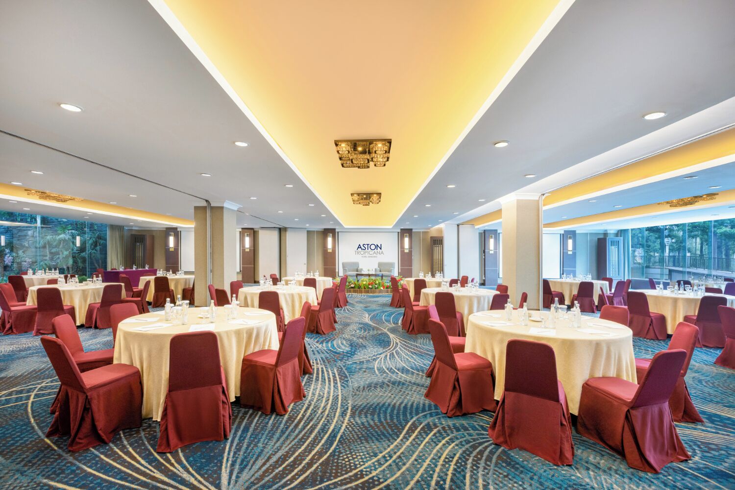 Un salón de conferencias con mesas redondas, sillas rojas y alfombra azul.