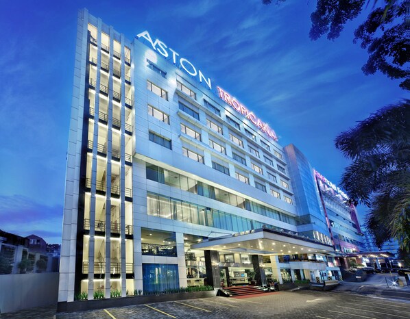 Un hotel de varios pisos con un llamativo letrero de "Aston", que presenta un diseño arquitectónico moderno con ventanas de vidrio y una entrada bien iluminada.