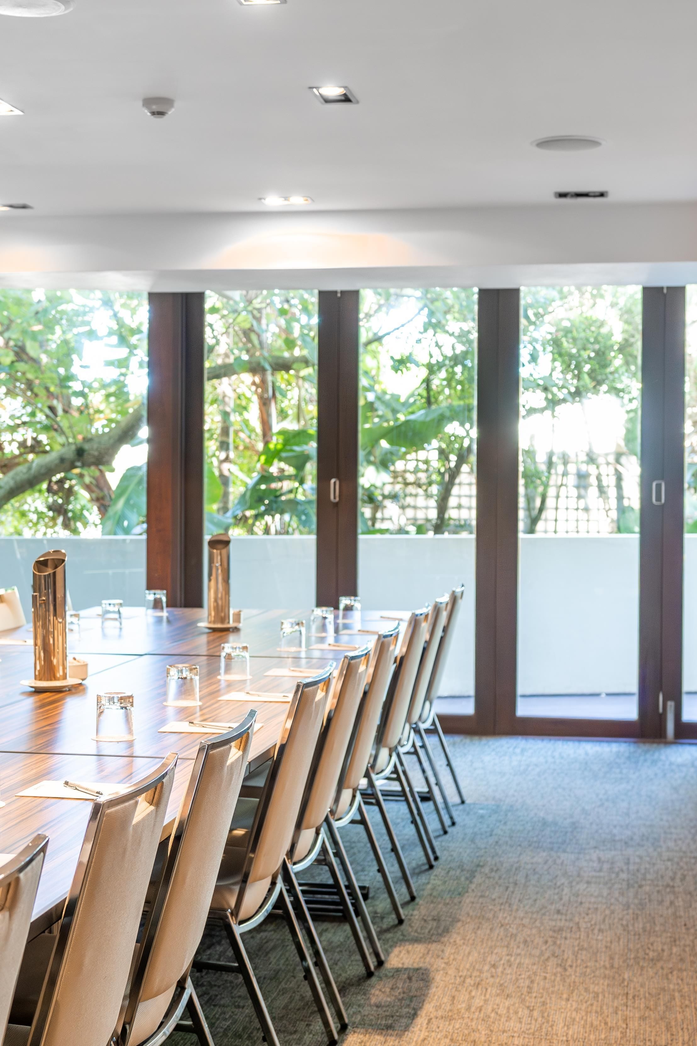 A conference room with a long table, chairs, and large windows with a view of greenery.