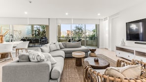 A modern living room with a sectional sofa, a TV, wicker chairs, and a dining area with a table and chairs.